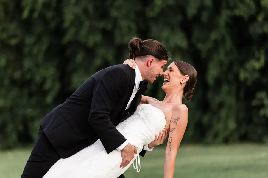 Novio inclinando a la novia en un abrazo romántico, ambos riendo