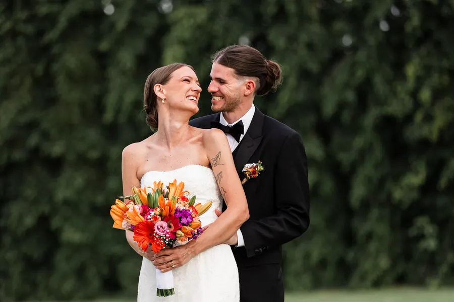 Novios abrazados mirándose con cariño, ella sostiene un ramo de flores coloridas